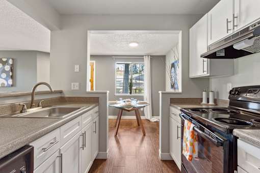 View of dining room with window from kitchen with wood-style flooring and white cabinets at Cedar Crest Apartments in West Beaverton, Oregon.