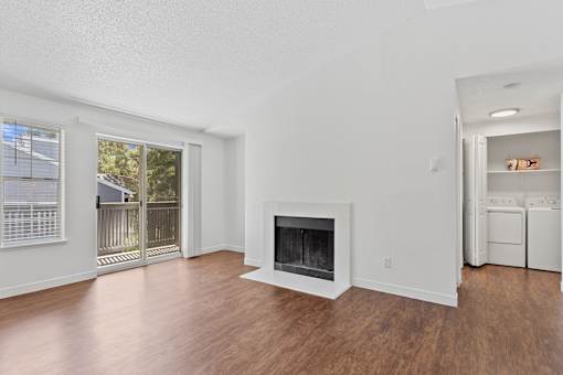 Living room with white walls, wood-style flooring, and large sliding glass door leading to outdoor patio at Cedar Crest Apartments in West Beaverton, Oregon.