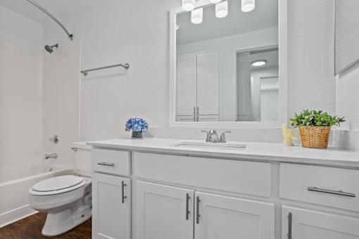 Bright bathroom with white walls, white cabinets, and large mirror at Cedar Crest Apartments in West Beaverton, Oregon.