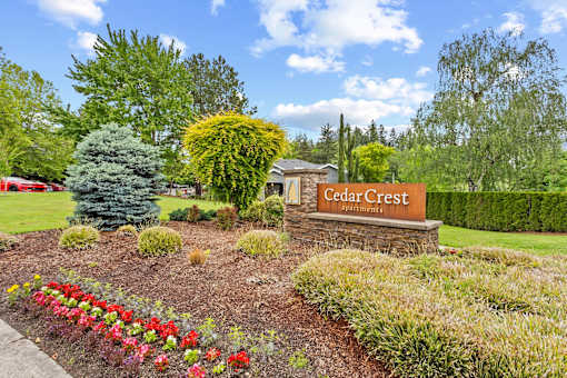 Front entrance monument sign with lush landscaping and flowers at Cedar Crest Apartments in West Beaverton, Oregon.
