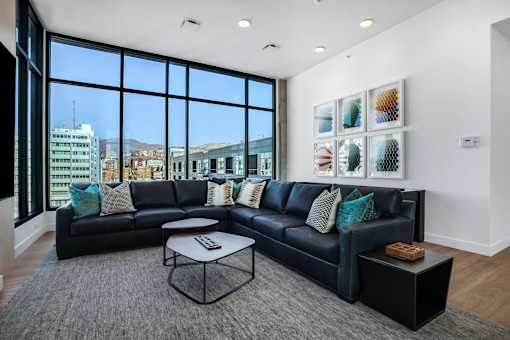 A black leather sofa with a grey rug and a coffee table in front of a window.