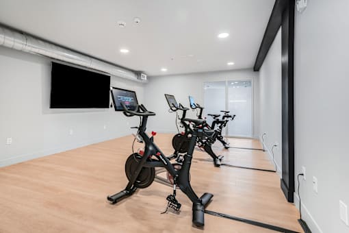 A room with a row of stationary bikes and a monitor on the wall.