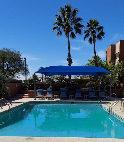 A pool with a blue umbrella and chairs under it.
