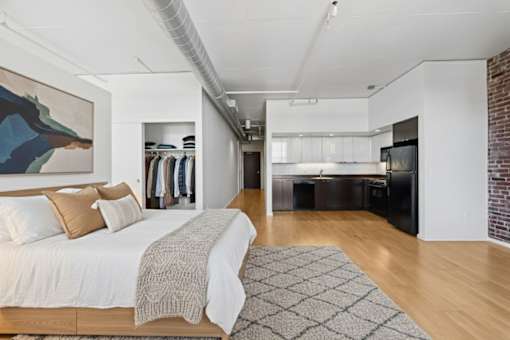 A studio with a large bed and a painting on the wall.