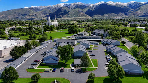 A large white building with a green lawn in front and mountains in the background.