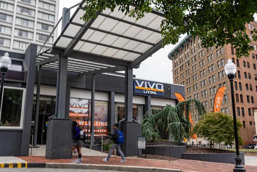 Two people are walking past a building with a sign that says "VIVO".