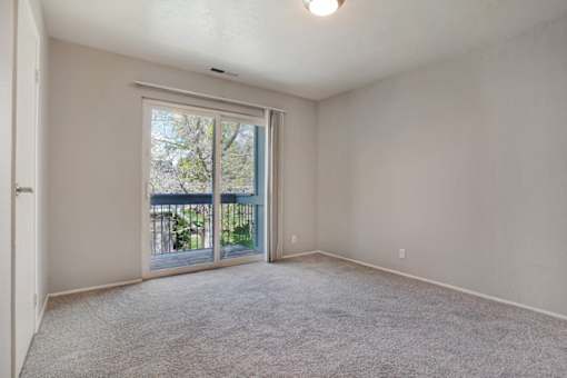 A room with a carpeted floor and a sliding glass door leading to a balcony.