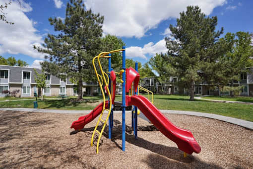 A red slide on a playground with a yellow ladder.