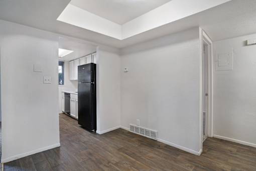 A black refrigerator sits in a kitchen with white walls and wood floors.