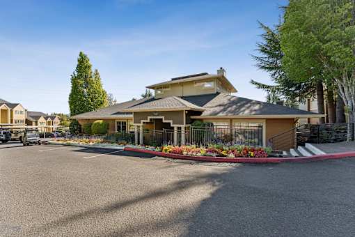 A large house with a grey roof and a red flower bed in front.