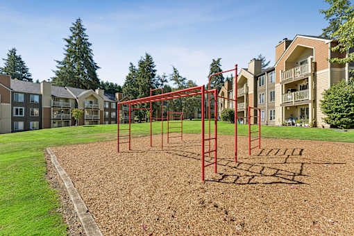 A playground with a red swing set in the middle of a grassy area.
