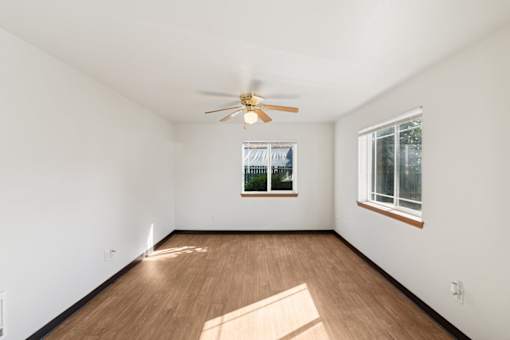 A room with a ceiling fan and two windows.