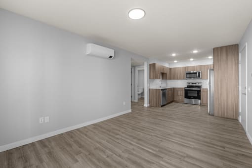 an empty living room and kitchen with wood flooring and white walls