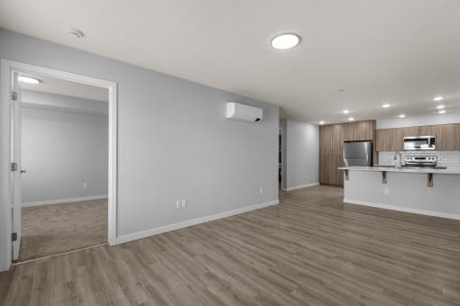an empty living room and kitchen with wood flooring and white walls