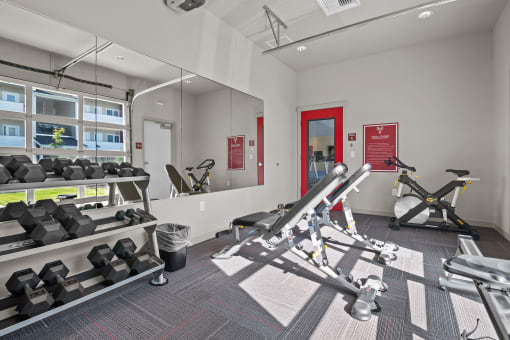 a gym with weights and mirrors at the district flats apartments in lenexa