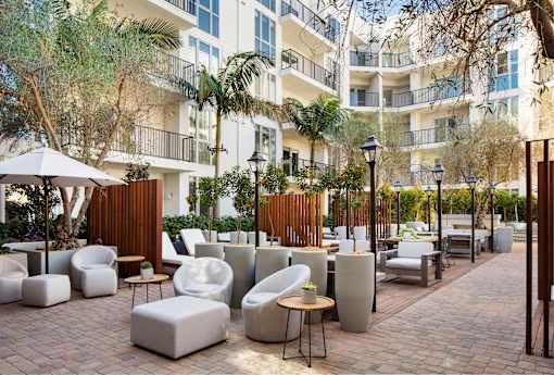 Dog-Friendly Apartments in Hollywood, CA - The Fifty Five Fifty - Courtyard with Palm Trees, White Outdoor Furniture, and Tall Wooden Dividers