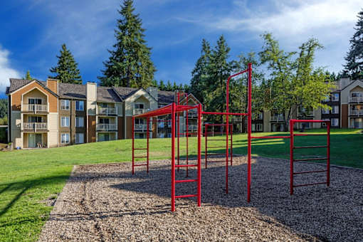 A red monkey bars set sits in the middle of a playground.