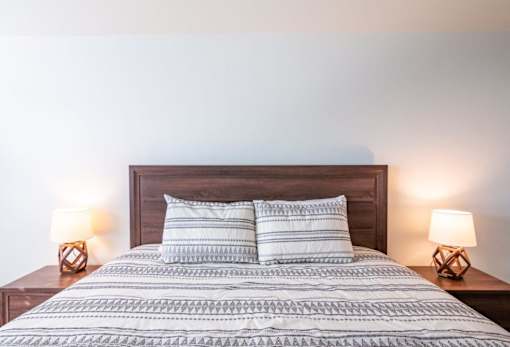 A bed with a wooden headboard and two pillows is flanked by two table lamps.