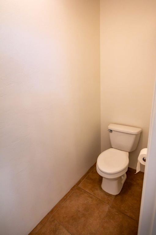 A white toilet in a small bathroom with brown tile flooring.