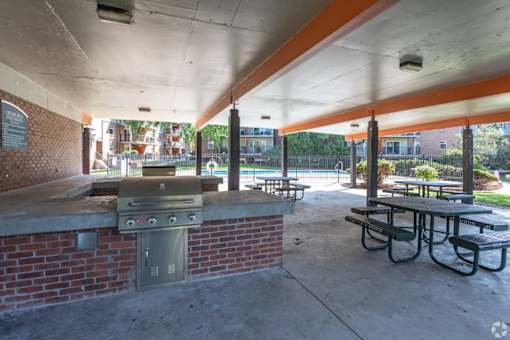 A covered picnic area with a grill and picnic tables.