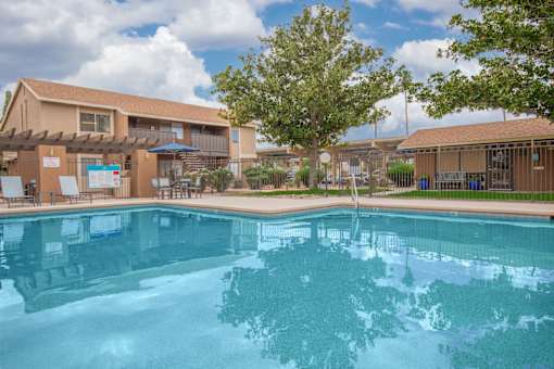 A swimming pool in front of a building with a blue sky and clouds in the background.