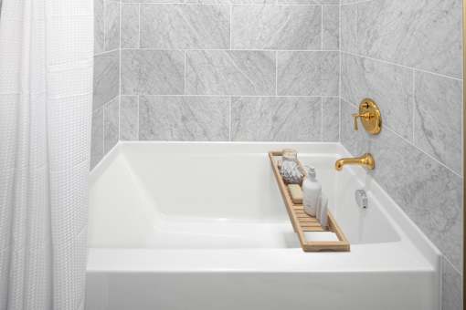 A white bathtub with a gold faucet and a tray with toiletries on it.