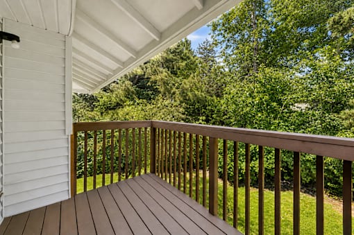 A wooden deck with a white house and trees in the background.
