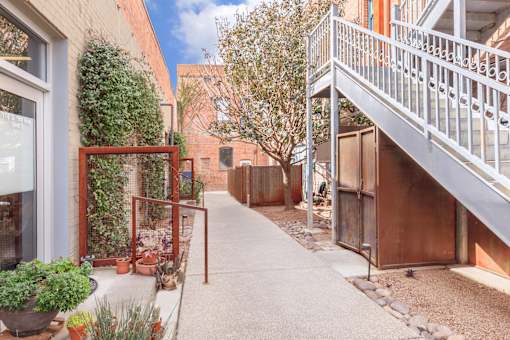 A narrow alley with a metal railing on the right and a red gate on the left.
