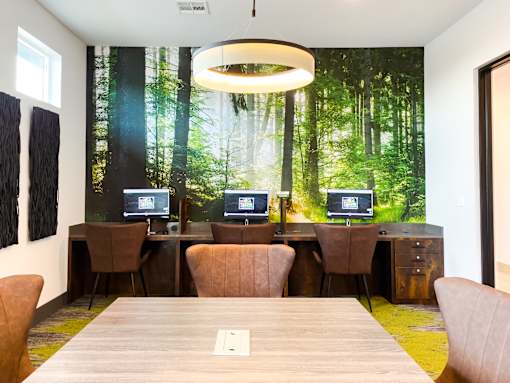 A conference room with a forest mural on the wall and four computers on desks.
