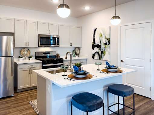 A modern kitchen with a white island and blue stools.