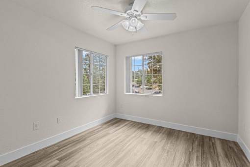 A room with a ceiling fan and two windows.