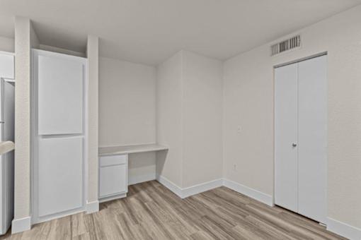 A white refrigerator is in a room with a wooden floor and white walls.