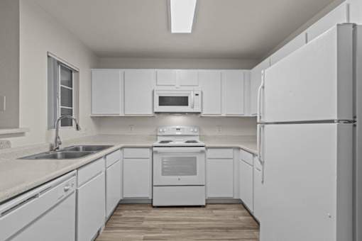 A white kitchen with a refrigerator, sink, and stove.