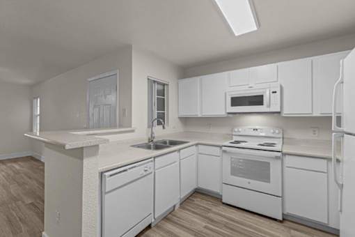 A white kitchen with wood flooring and white appliances.