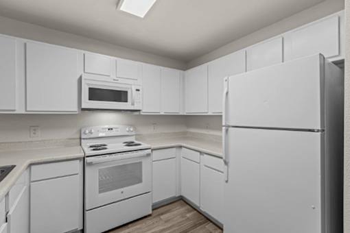 A white kitchen with a stove, microwave, and refrigerator.