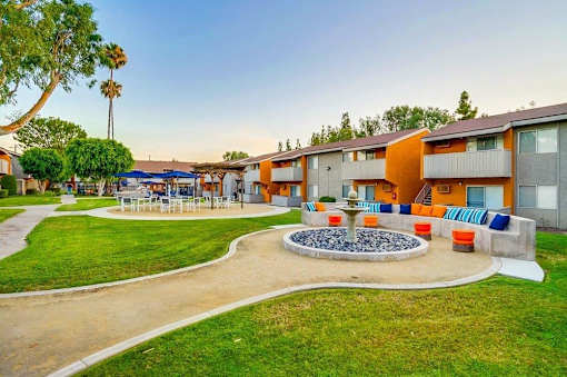 A sunny day at a park with a fountain in the middle of a grassy area.