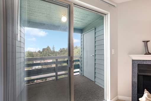 A glass door leading to a balcony with a view of a parking lot and trees.