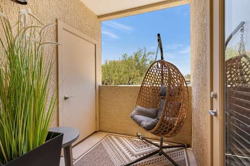 A hanging chair is suspended from a hook in a room with a view of the outdoors.