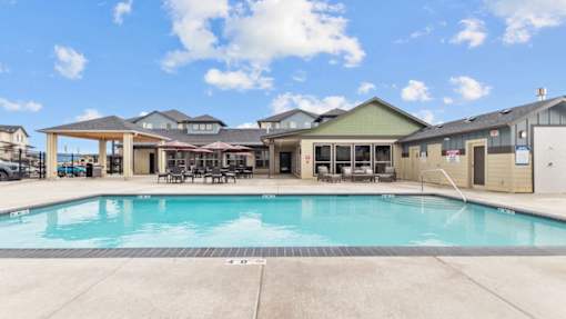 A large swimming pool in front of a building with a covered patio area.