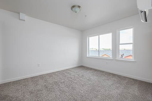 an empty living room with three windows and carpeting