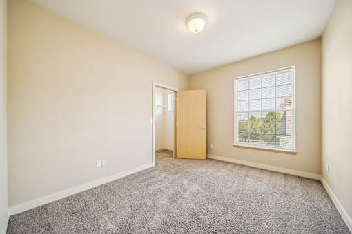 A room with a carpeted floor, a door, and a window.