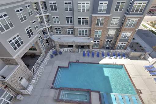 A large swimming pool is surrounded by a patio with lounge chairs and a stone building with a balcony.