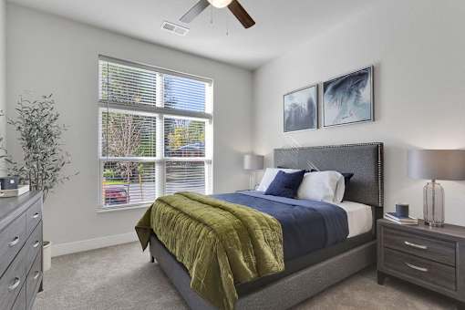 A bedroom with a bed, nightstand, and window with blinds.