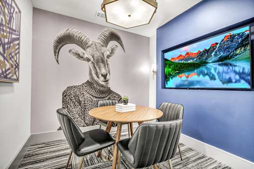 A room with a table, chairs, and a large screen displaying a mountain landscape.