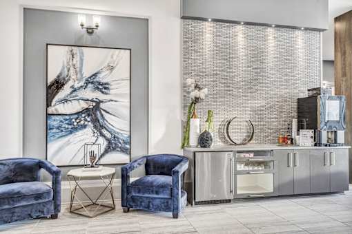 A modern living room with blue velvet chairs and a large abstract painting.