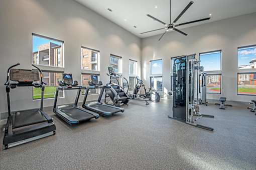 A spacious gym with treadmills, elliptical machines, and a fan.
