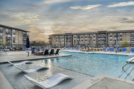 A swimming pool with a slide and loungers in front of apartment buildings.