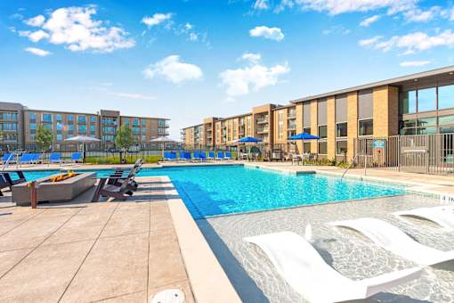 A swimming pool with sun loungers and apartment buildings in the background.