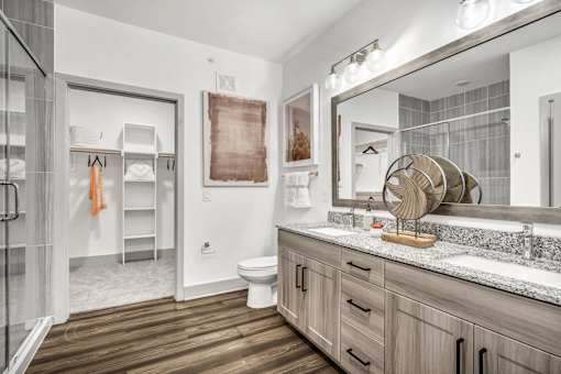 A bathroom with a white toilet, a wooden floor, and a large mirror.