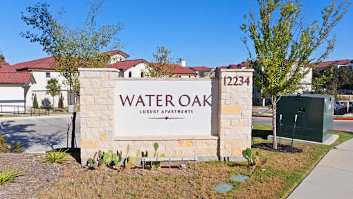 A sign for Water Oak Luxury Apartments is displayed in front of a building.